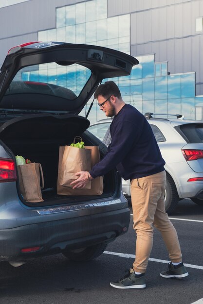 Happy man put groceries bag in car trunk