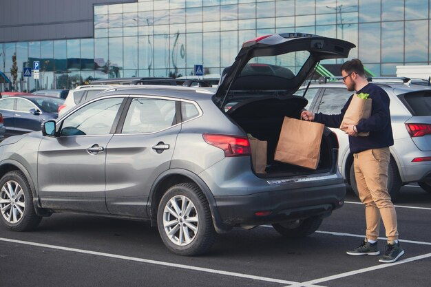 Happy man put groceries bag in car trunk