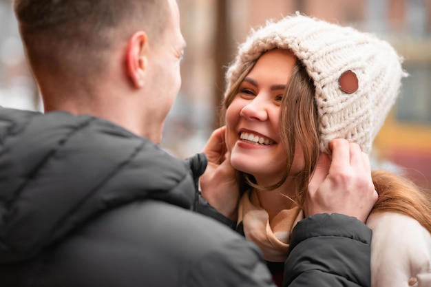 Happy man puts on a winter hat for his woman. The guy in love takes care of the girl. Happy healthy couple outdoors enjoying life