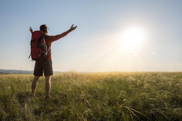 Happy man raised hands at sunset on the summer meadow Tourist man hiker travelling at nature Active life freedom concept