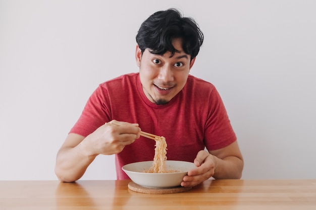 赤いTシャツの幸せな男は白い背景のインスタントラーメンを食べる