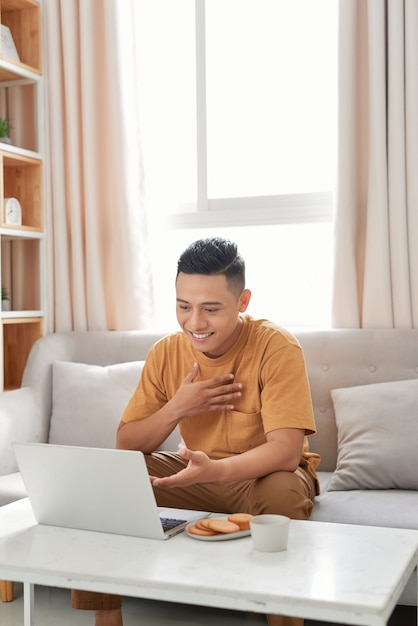 Счастливый человек расслабляется на диване во время видеозвонка с помощью ноутбука дома