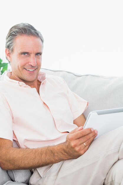 Happy man relaxing on his couch using tablet pc looking at camera