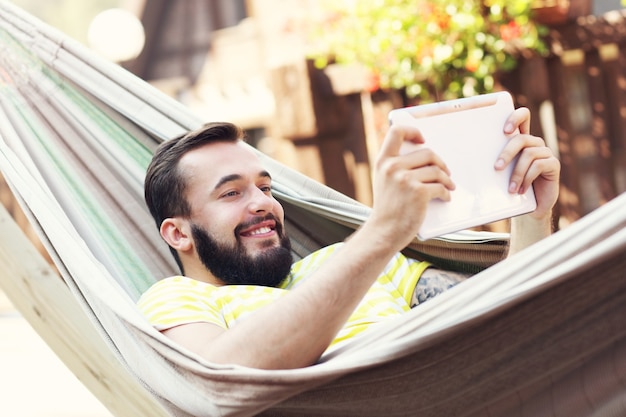 happy man resting on hammock with tablet