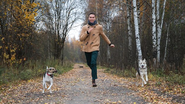 Uomo felice che corre in direzione della telecamera con due cani all'esterno