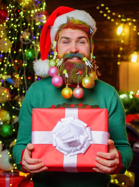 Happy man in santa hat with decorated beard and christmas gift new year holidays funny wintertime