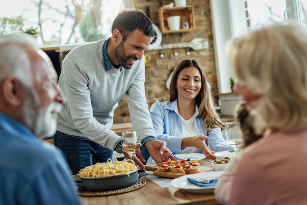 Uomo felice che serve antipasto mentre pranza con la sua famiglia nella sala da pranzo