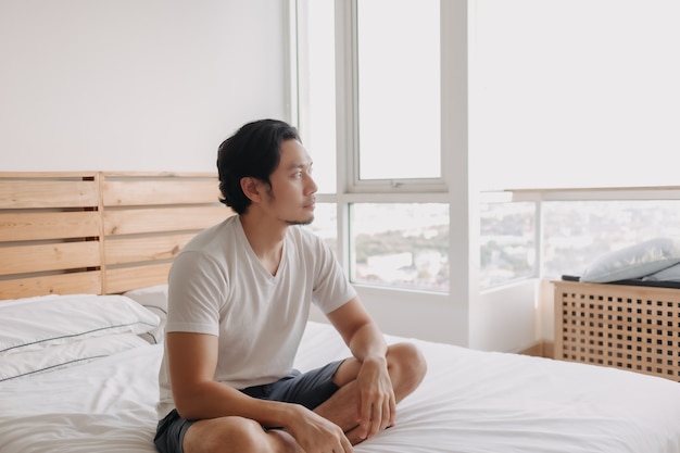 Happy man sits and relax on his bed in his apartment