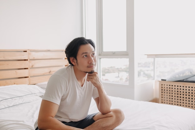 Happy man sits and relax on his bed in his apartment