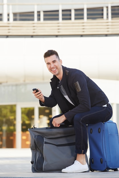 Happy man sitting on luggage with cellphone waiting