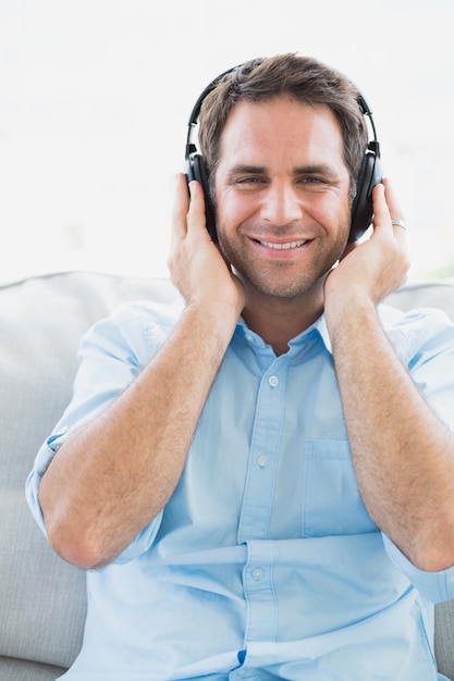 Happy man sitting on sofa listening to music smiling at camera