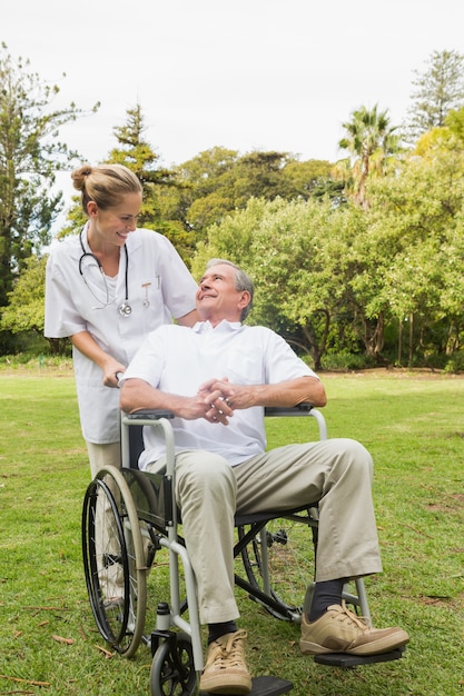 Happy man sitting in a wheelchair talking with his nurse pushing him