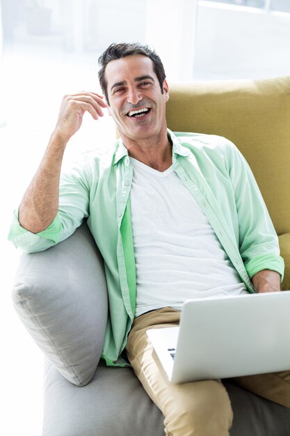 Счастливый человек сидит с ноутбуком на диване