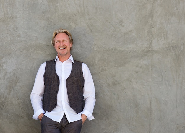 Happy man smiling with hands in pocket against a wall