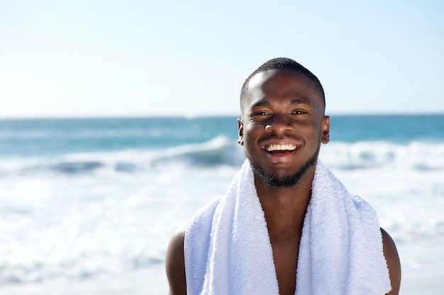 Uomo felice che sorride con un asciugamano in spiaggia