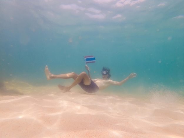 Счастливый человек в маске для подводного плавания ныряет под воду с тропическими рыбами с флагом Таиланда в морском бассейне с коралловым рифом