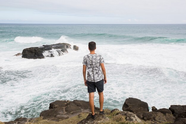 山の頂上に立って、海を見下ろす幸せな男。成功、勝者、幸福。