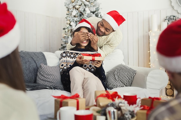 행복한 남자는 크리스마스 선물로 소녀를 놀라게 하고, 뒤에서 눈을 감고, 겨울 휴가를 즐기고, 공간을 복사합니다.