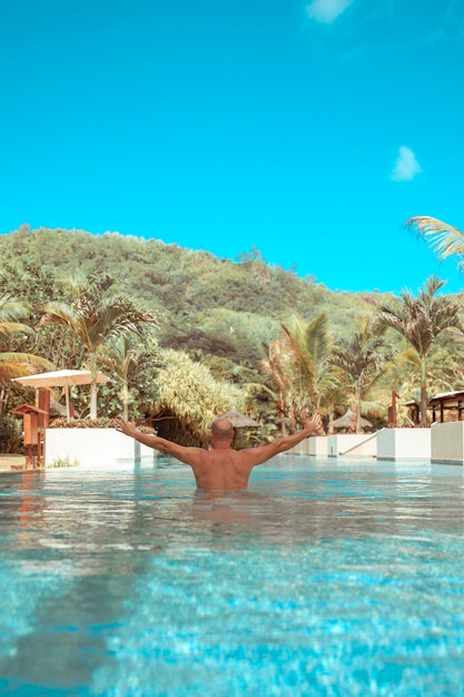 счастливый мужчина плавает в бассейне на Сейшельских островах концепция летних каникул
