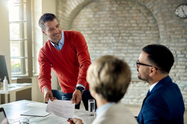 Happy man talking to business people while giving them his resume during a job interview in the office