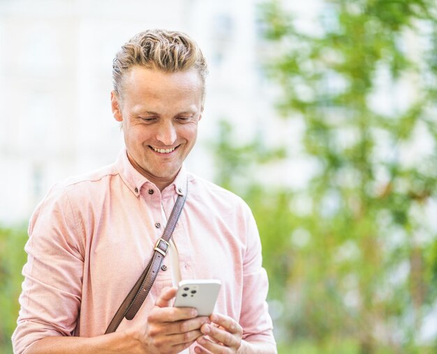 Happy man texting message on phone while standing across street in urban city concept of easy commun