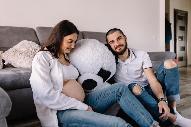 Happy man touching belly of smiling pregnant woman lying on sofa