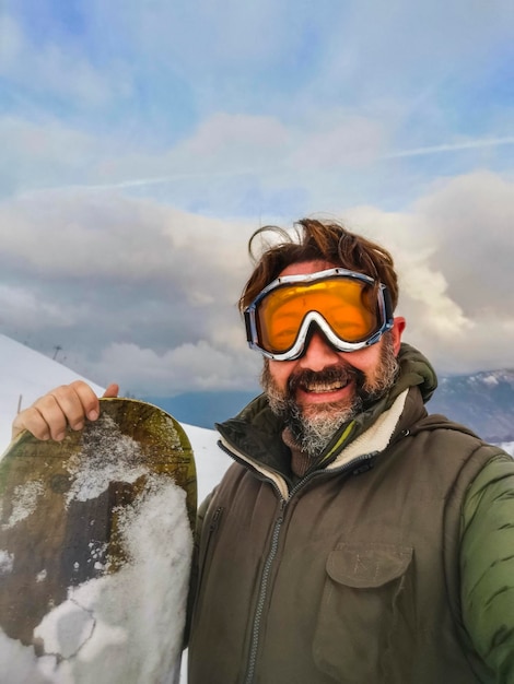 Happy man tourist in snow mountain taking selfie picture Adult mature people in yong sport activity Senior doing snowboard with youthful smile Mountains and snow in backgorund