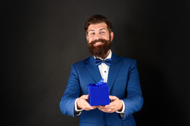 Happy man in tuxedo bow tie formalwear on black background\
presenting box shopping sale