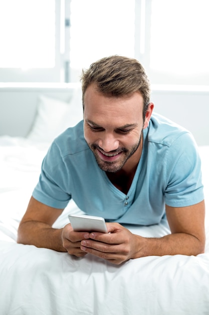 Happy man using cellphone while lying on bed