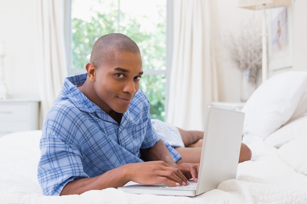 Uomo felice che per mezzo del computer portatile sul letto