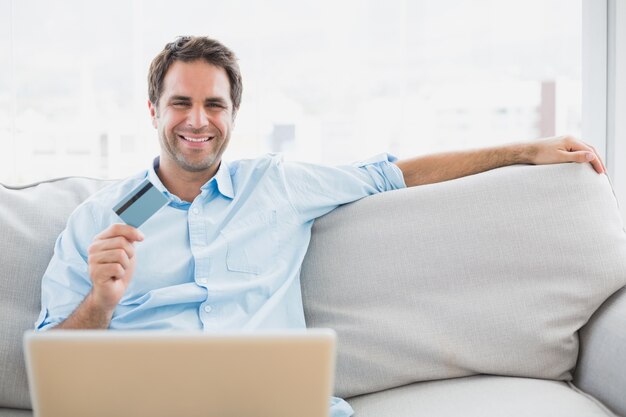 Happy man using laptop sitting on sofa shopping online