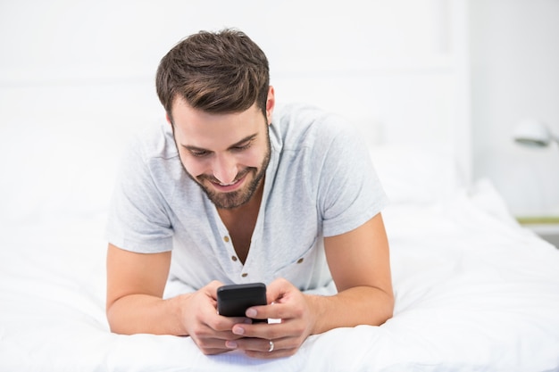 Uomo felice che per mezzo del telefono cellulare sul letto