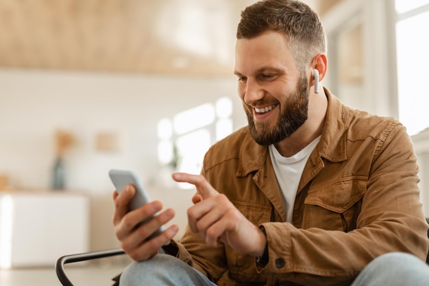 Happy man using mobile phone wearing earbuds texting at home