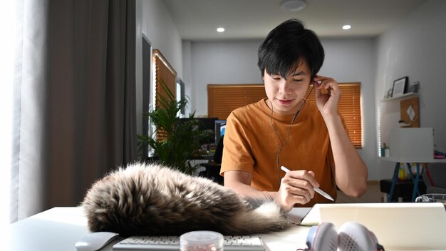 Happy man wearing earphones and working with digital table at home