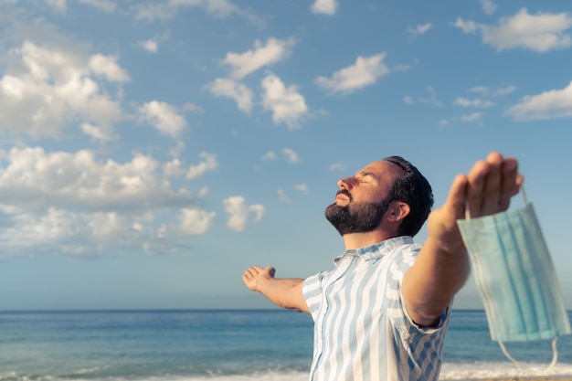 Uomo felice che indossa maschera medica all'aperto contro il cielo blu sullo sfondo