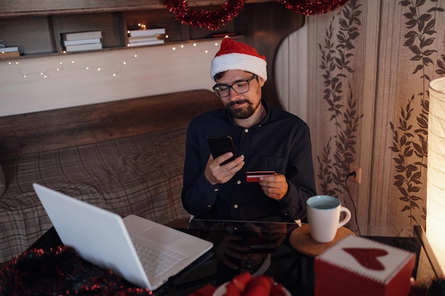 Uomo felice che indossa il cappello di babbo natale che tiene un regalo o una carta di credito