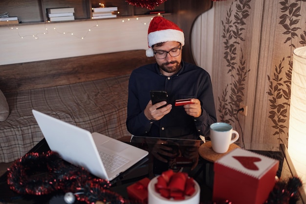 Uomo felice che indossa il cappello di babbo natale che tiene un regalo o una carta di credito