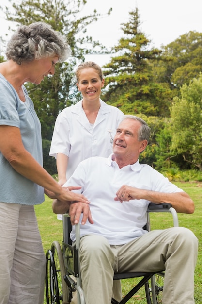 Счастливый человек в инвалидной коляске разговаривает со своей медсестрой и женой