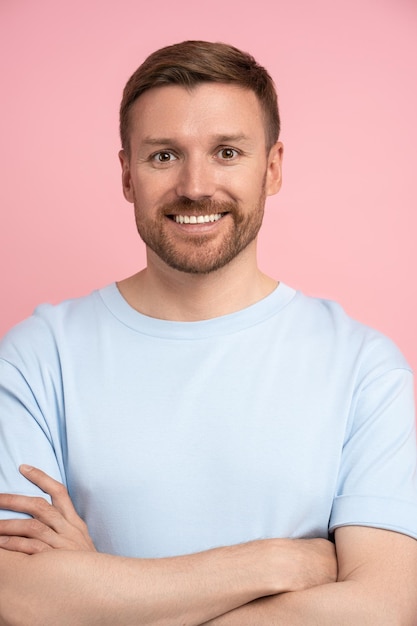 Happy man white teeth smiling with crossed arms look at camera standing isolated on pink studio wall