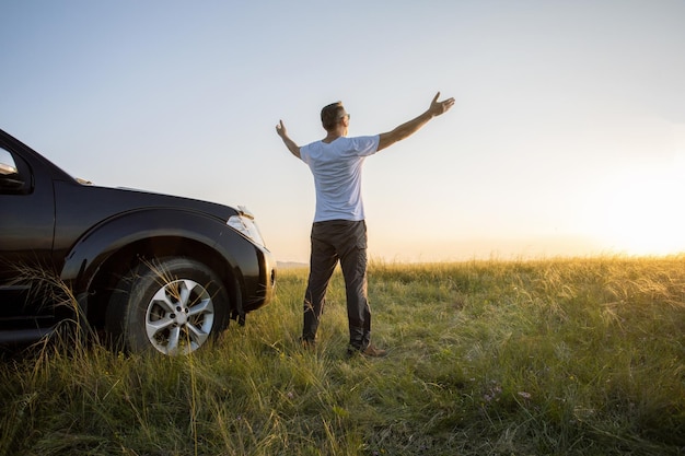 Happy man with arms up standing near his car and watching the sunset travel summer vacation freedom concept