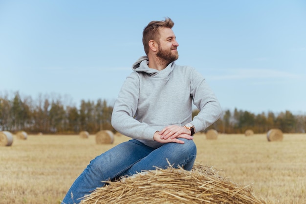 パーカーにひげを生やした幸せな男は干し草の山に座っています。