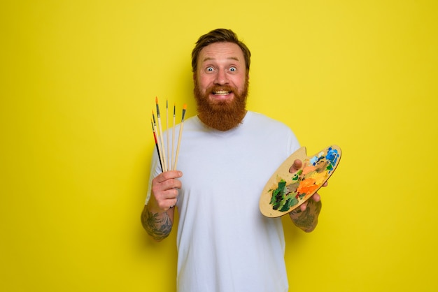 Happy man with beard and tattoo is ready to draw with brushes