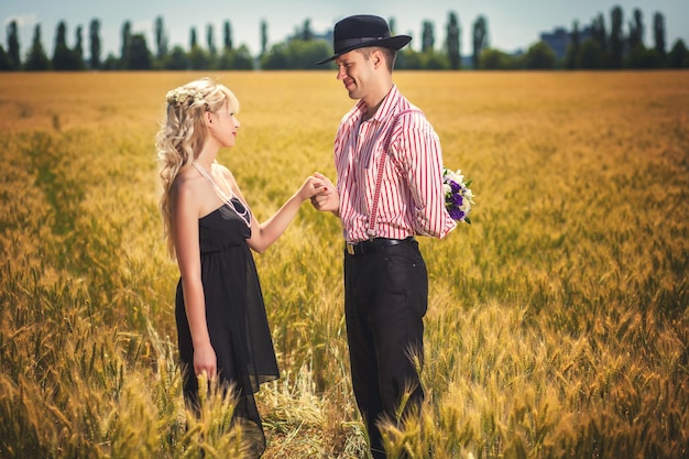 Happy man with bouquet behind his back and woman on wheat field