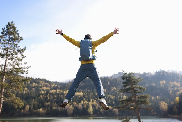 Happy man with open arms jumping lake and mountains in background hiker with backpack