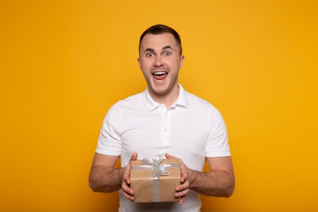 Happy man with open mouth holding present on yellow