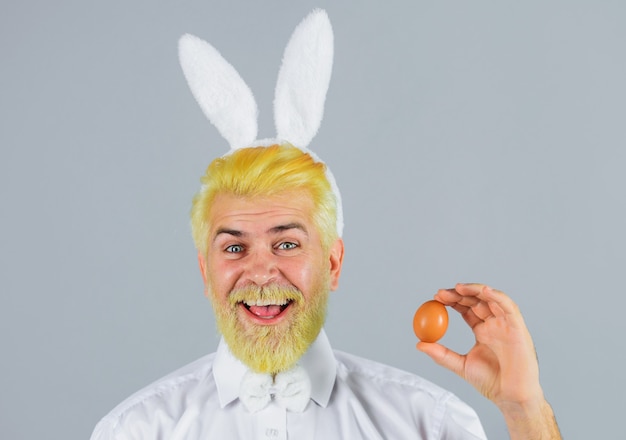 Happy man with rabbit ears holing a easter egg on grey background.