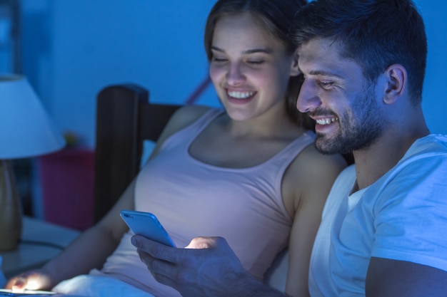 Il telefono felice dell'uomo e della donna in camera da letto. notte