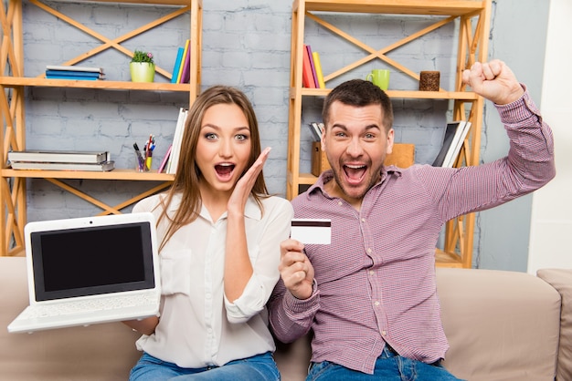 Happy man and woman screaming with laptop and bank card