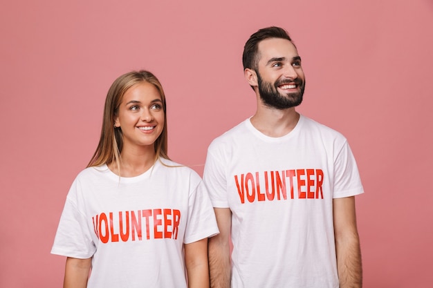 happy man and woman volunteers wearing uniform t-shirts looking at copyspace isolated