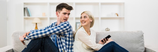 The happy man and woman with a phone and a tablet sit on the sofa